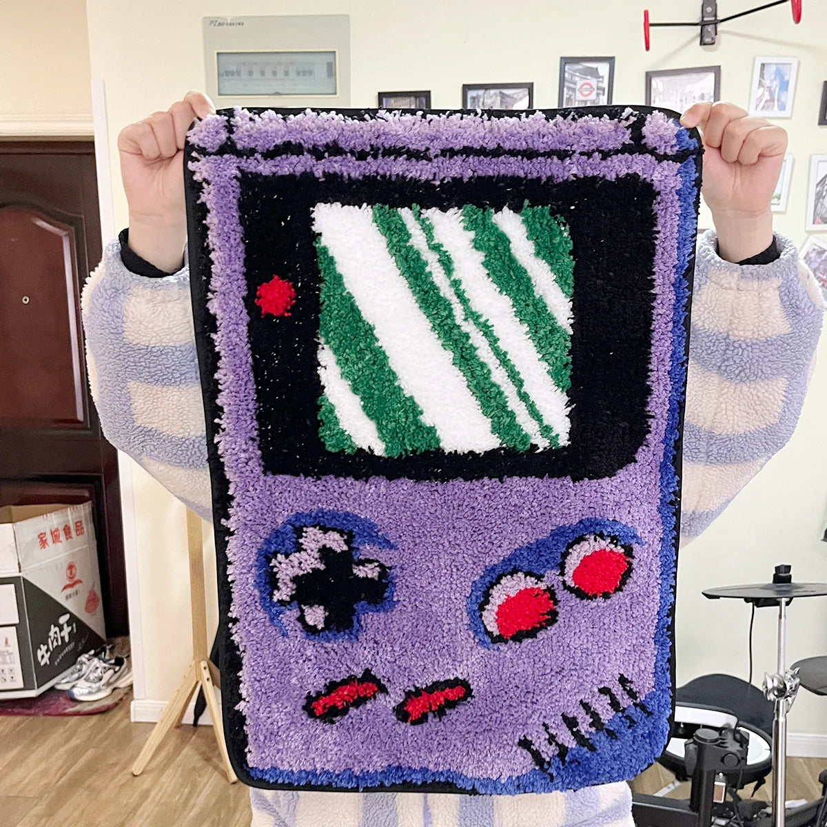 A purple tufted floor mat featuring a black frame and green striped design is held up by a person.