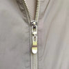 Close-up of a silver metal zipper pull on a gray fabric, showing the zipper teeth and pull mechanism.