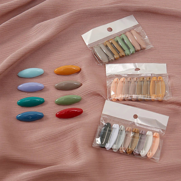 Eight plastic safety pins in various colors are displayed on a pink fabric with individual packaging.
