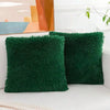Two emerald green faux fur throw pillows resting on a white surface next to an abstract painting.