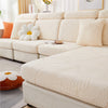 A cream colored leaf jacquard stretch sofa cover displayed on a light-colored sofa with white decorative pillows.