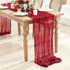 A deep red semi-sheer gauze table runner draped elegantly on a wooden dining table set for a meal.