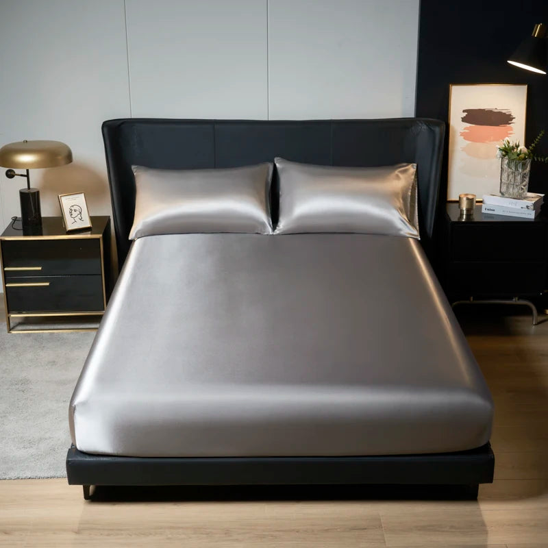 A modern bedroom featuring a bed dressed in silver satin bedding and dark gray linens.