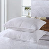 A stack of white embroidered cotton quilted pillow covers on a bed with a window view.