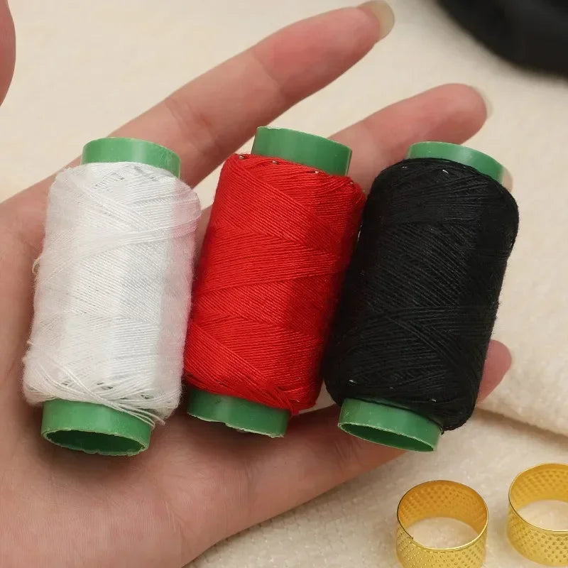 A hand holds a set of three colored sewing thread spools: white, red, and black, with green caps visible.