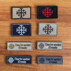 A collection of black and gray embroidered patches featuring a cross design, some with text related to the Crusades.