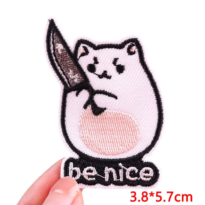 Pink embroidered patch of a cat holding a knife with the text be nice