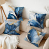 A collection of abstract leaf pattern cushion pillow covers in shades of blue, white, and gold on a beige sofa.