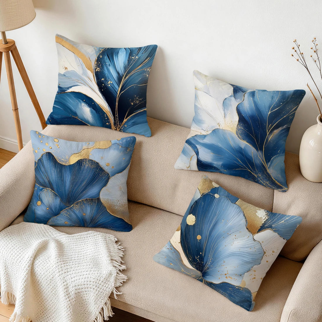 A collection of abstract leaf pattern cushion pillow covers in shades of blue, white, and gold on a beige sofa.
