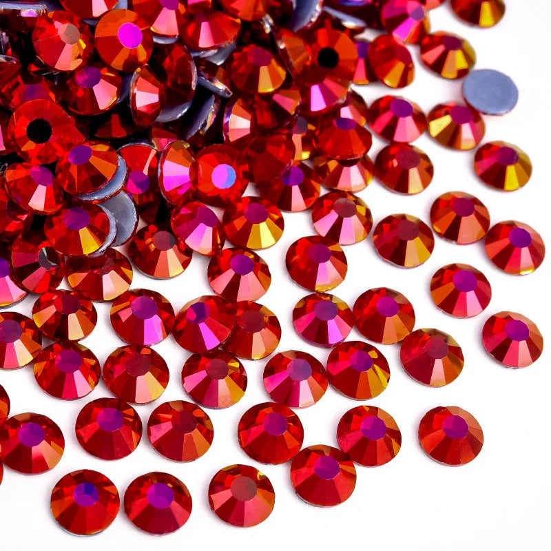 A pile of red and pink flatback glass rhinestones scattered on a white background.