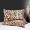 Two leopard print silk satin pillowcases in beige and black spots resting on a white surface.
