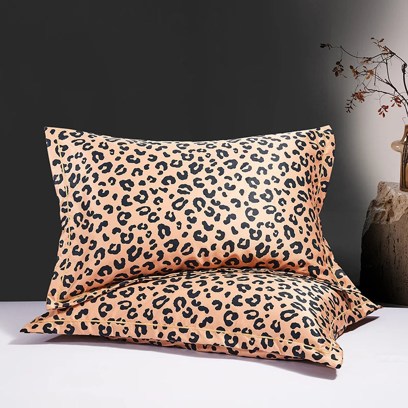 Two leopard print silk satin pillowcases in beige and black spots resting on a white surface.
