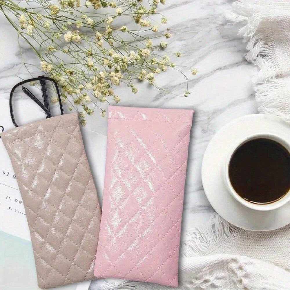 Pink and beige suede-like squeeze-top PU leather eyeglass case with a cleaning cloth next to a cup of coffee