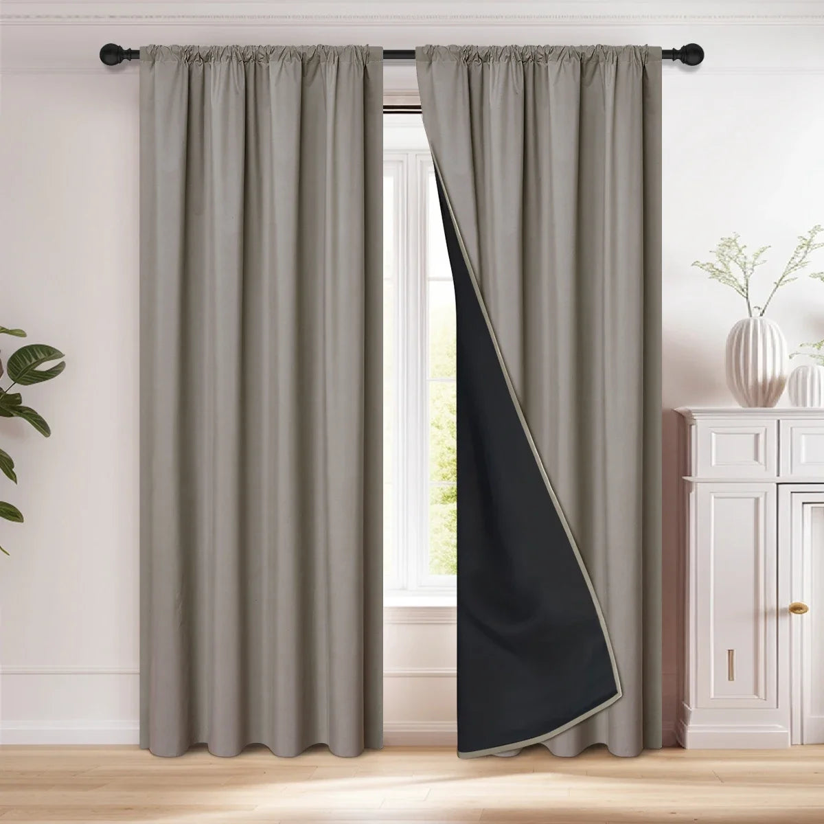 A floor-length gray blackout curtain with a black diagonal panel hanging in a window frame.