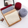 A collection of hand-knitted yarn in various shades of gray, red, and beige is displayed in a wooden box.
