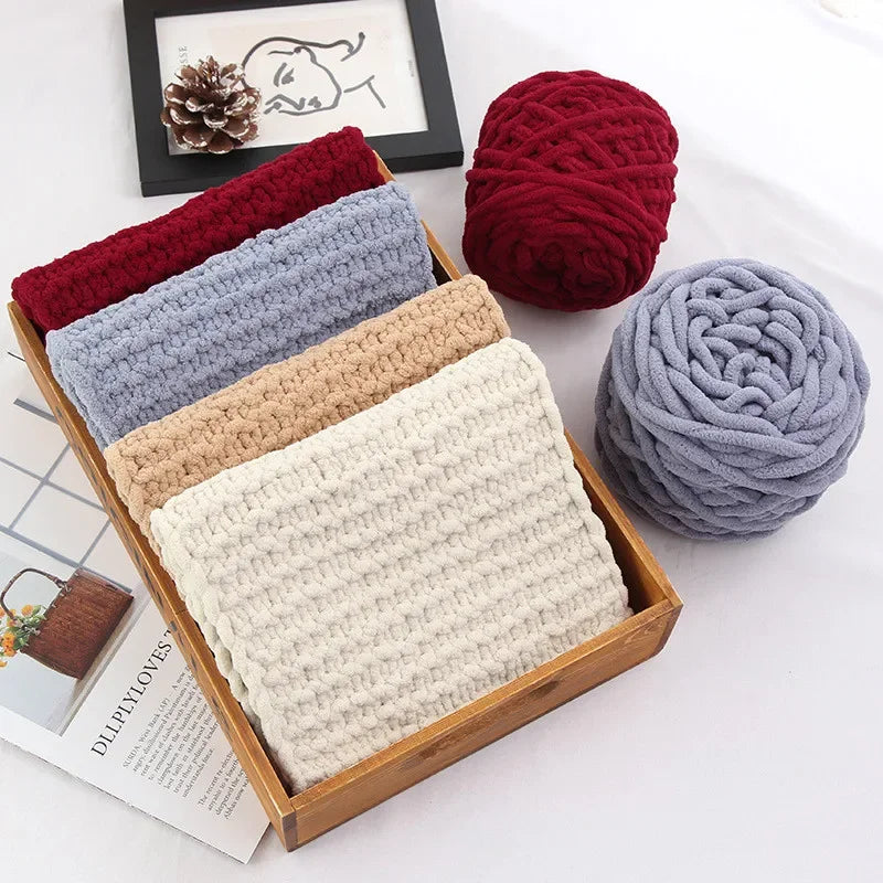 A collection of hand-knitted yarn in various shades of gray, red, and beige is displayed in a wooden box.