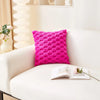 A bright pink, textured plush pillow resting on a white sofa next to an open book.