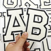 A hand is holding a black and white letter patch, specifically the letter B, which is part of a set for clothing decoration.