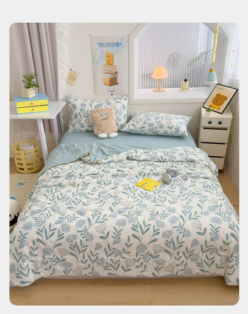 A light blue and white patterned quilt with floral embroidery is displayed on a bed, surrounded by decorative items.