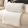 A rolled white flannel throw blanket resting on a light-colored sofa.