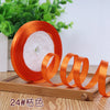 Orange satin ribbon rolled around a white candle on a wooden board