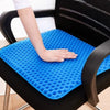 A hand rests on a blue honeycomb silicone seat cushion placed on a black chair.