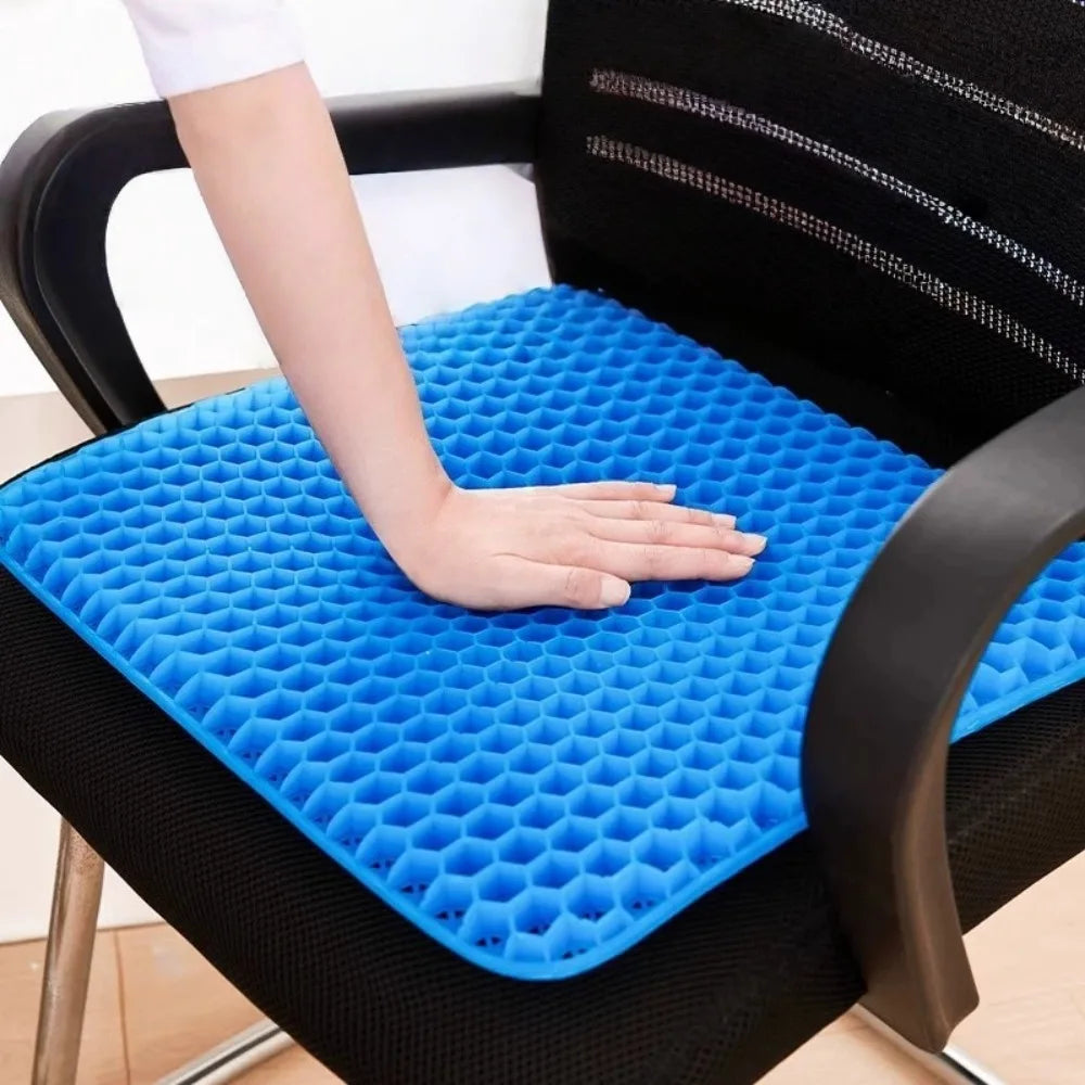 A hand rests on a blue honeycomb silicone seat cushion placed on a black chair.