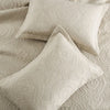 A set of light beige embroidered cotton quilted pillow covers resting on a textured fabric surface.