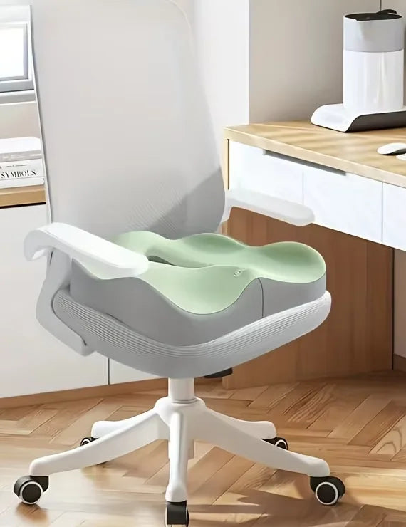 A light gray ergonomic memory foam seat cushion with a green backrest is shown on a white office chair.