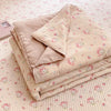 A stack of light pink cartoon quilting comforters with small pink animal designs resting on a quilted surface.