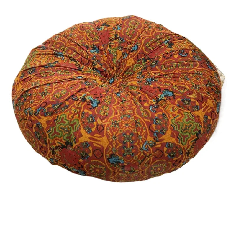 A round throw cushion with an orange and red bohemian pattern.