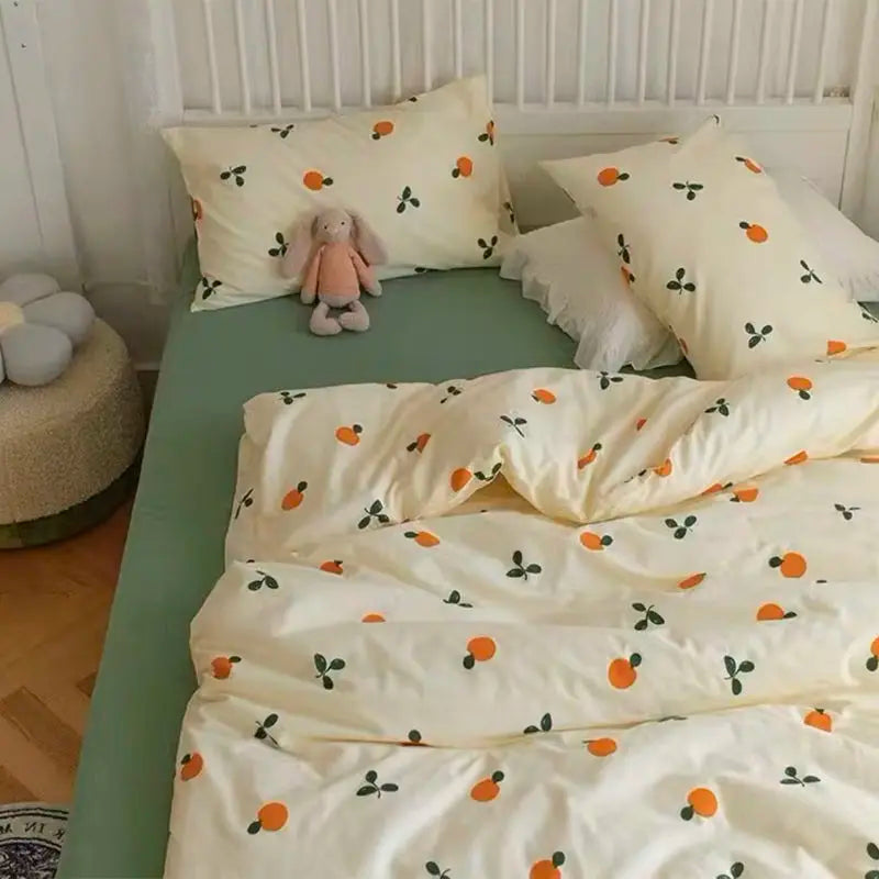 A light yellow bedding set with a pattern of small orange and green leaves is displayed on a bed.