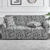 A gray floral print elastic sofa cover protector displayed on a light gray rug.