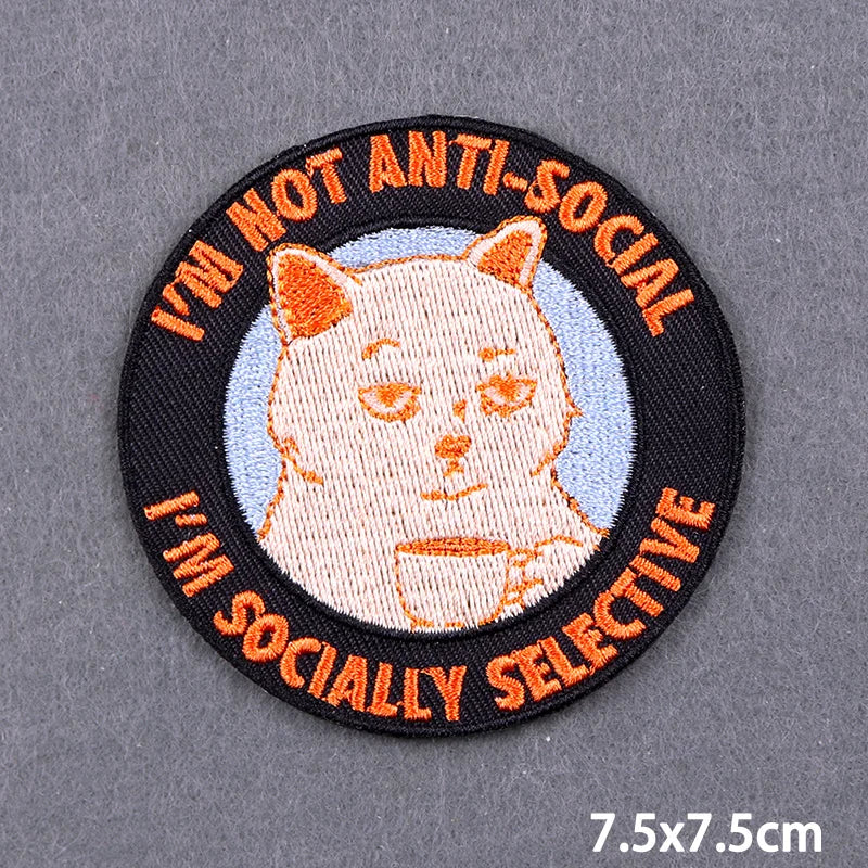 Black embroidery patch with orange text and a white cat face design on a light blue background