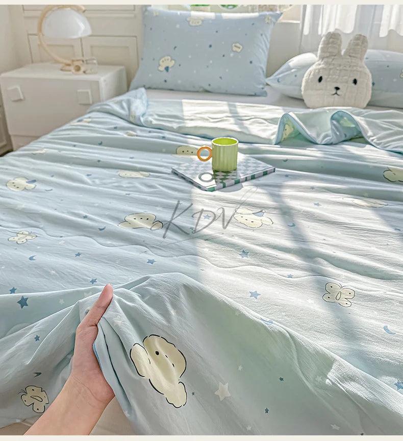 A light blue quilt blanket with a pastoral print featuring small white animals and stars, displayed on a bed.