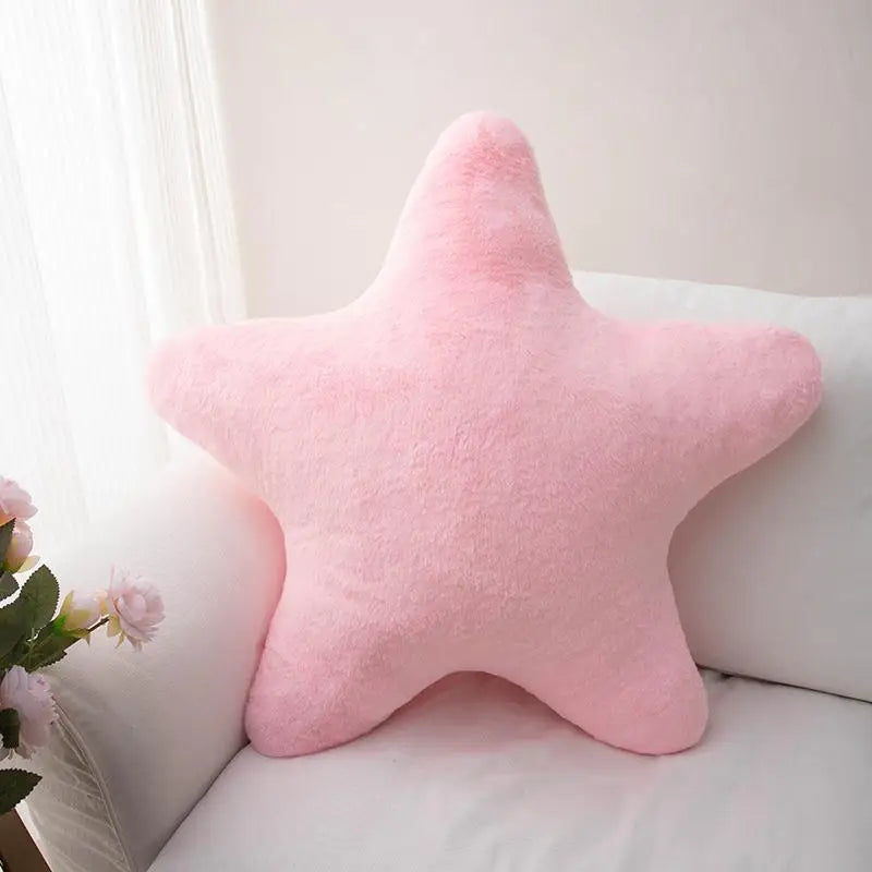A pink star-shaped plush throw pillow resting on a white sofa.