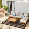 A light gray outdoor patio rug with a black geometric pattern placed on a wooden deck next to a white stucco wall.