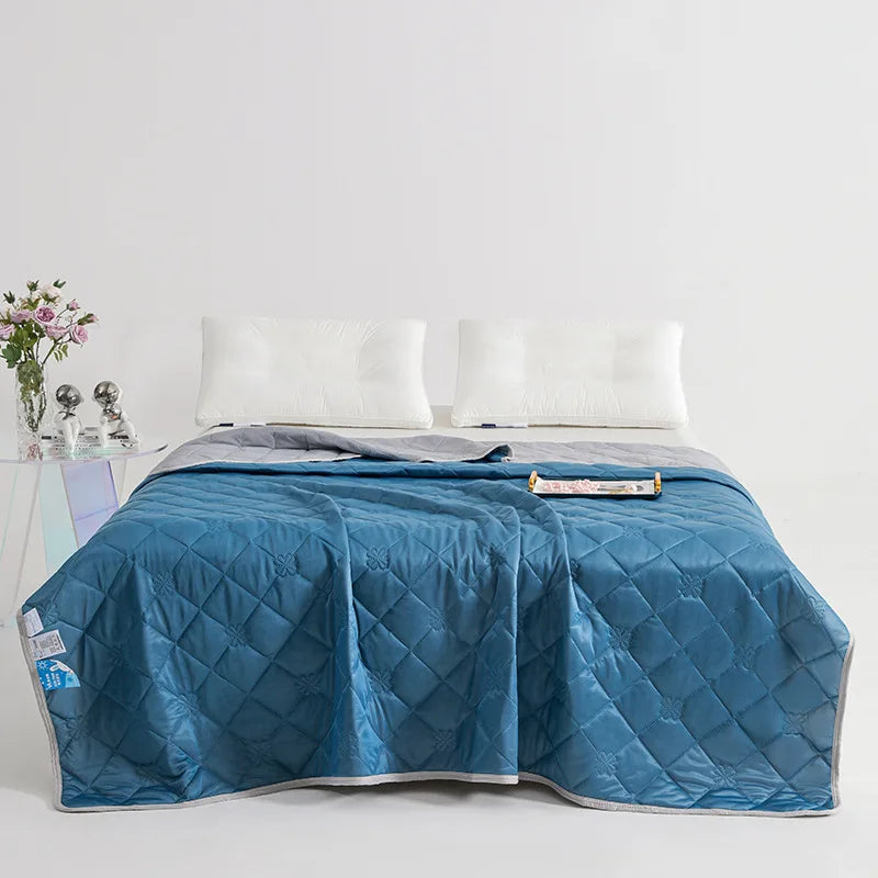 A deep blue quilted blanket is spread on a bed with white pillows and a light-colored side table.