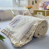A rolled light beige quilt blanket with a subtle floral print texture is displayed on a white surface.
