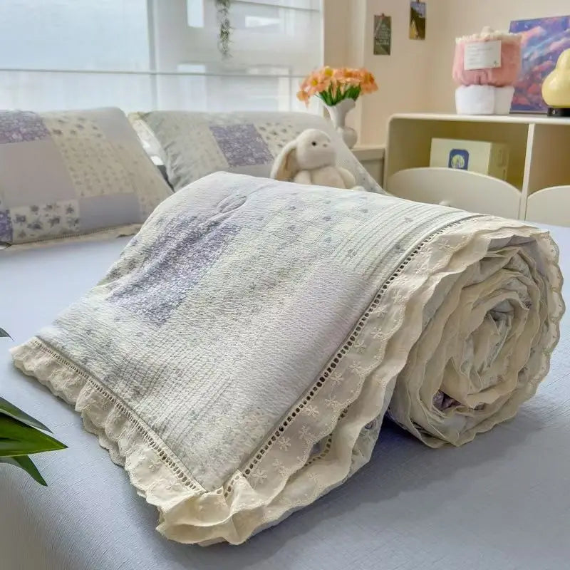 A rolled light beige quilt blanket with a subtle floral print texture is displayed on a white surface.
