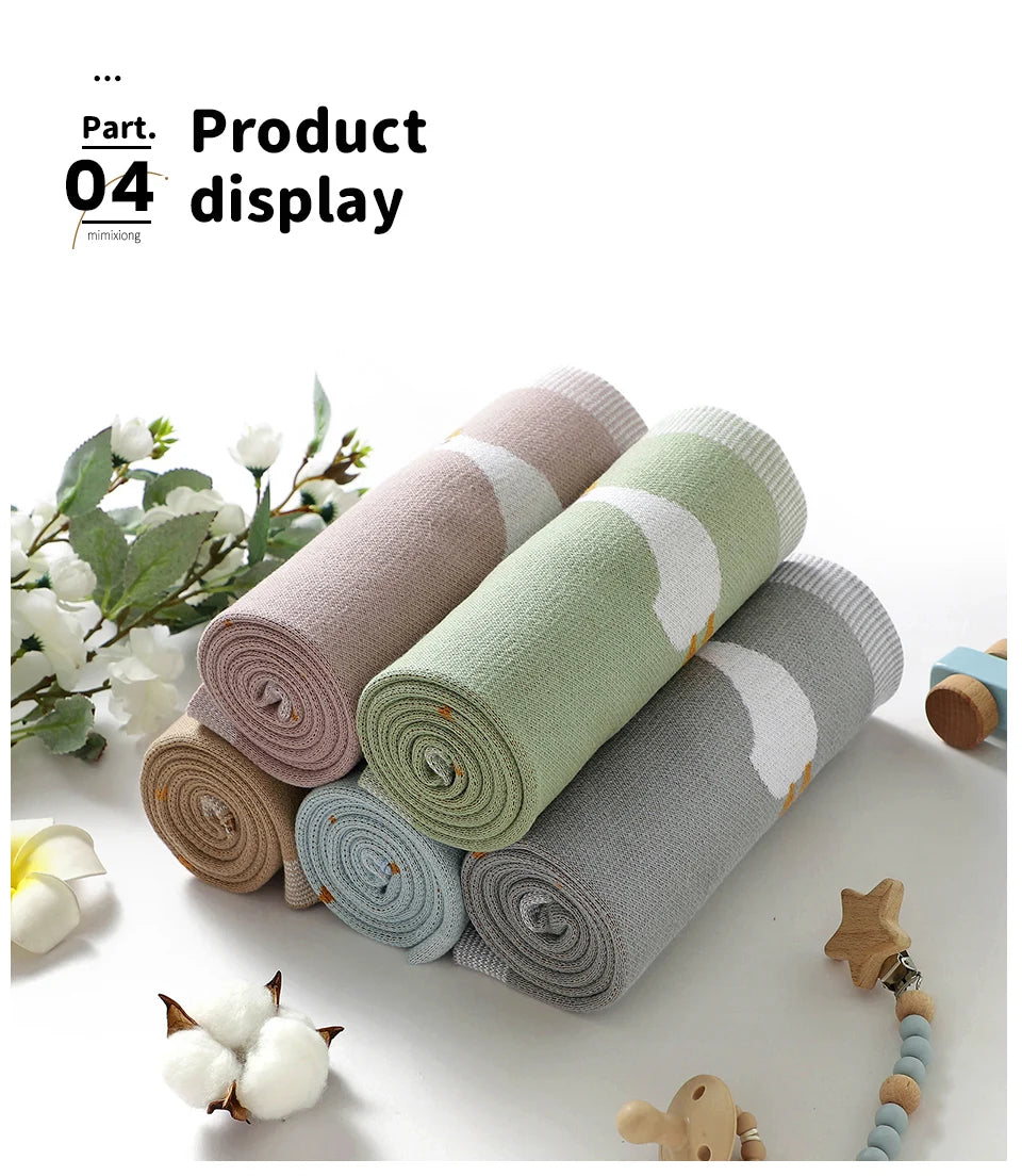 A set of four rolled cotton infant blankets and swaddles in various muted tones like beige, sage green, and gray.