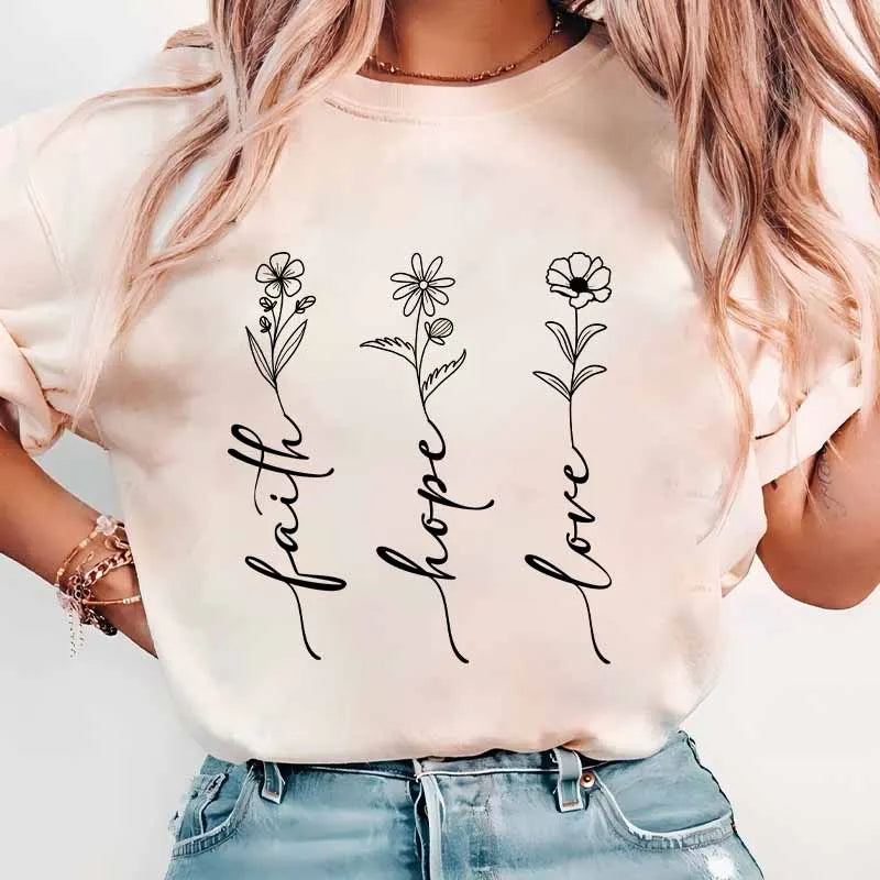 A close-up of a light pink t-shirt featuring black line art designs of faith hope and love flowers.