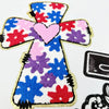 A colorful cross shape made of embroidered patches in red, blue, purple, and pink.