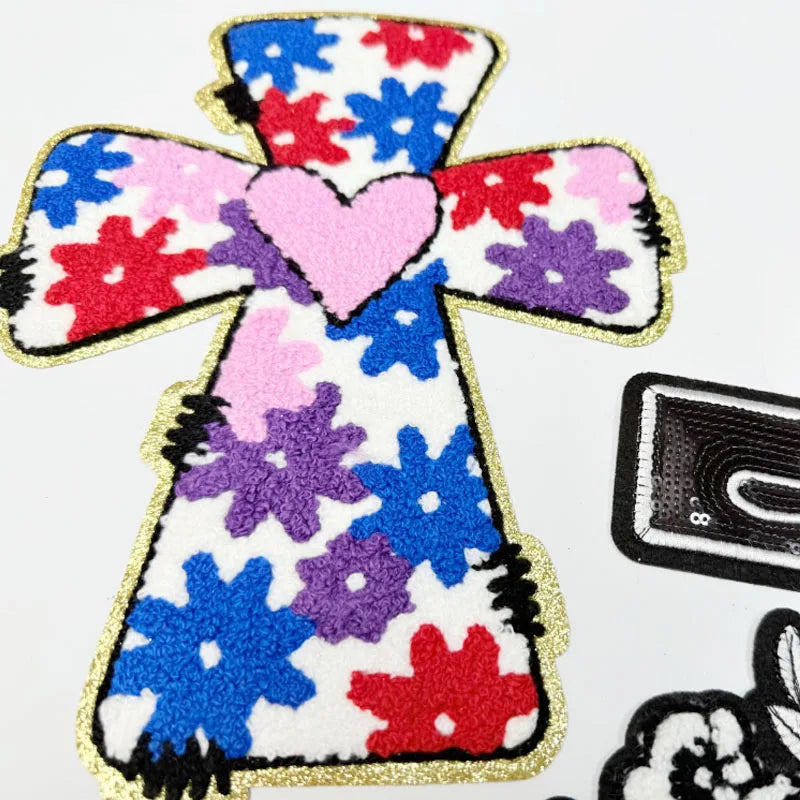 A colorful cross shape made of embroidered patches in red, blue, purple, and pink.