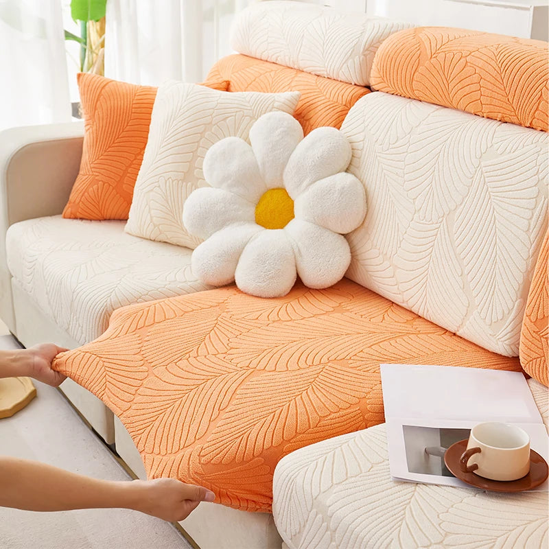 An orange leaf jacquard stretch sofa cover with white pillows and a yellow flower accent