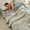 A woman is relaxing under a striped light blue and white quilt in a bed.