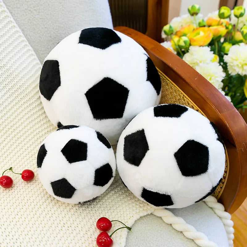 A white and black realistic football plush toy resting on a woven tray next to yellow and white flowers.