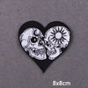 Black heart-shaped iron-on patch featuring white embroidered skulls