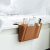 A brown felt storage organizer with hanging pockets holding several smartphones and cards on a white bedside table.