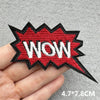 A hand holds a red and black embroidered speech bubble patch with the word WOW on it.